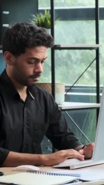 Orta Doğulu neşeli iş adamı ofiste bilgisayarla çalışırken başarıyı kutluyor ve sandalyeye yaslanıyor. Dikey video.