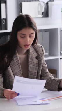 Ofiste çalışırken evrak işleriyle, bilgi analizleriyle ve iş muhasebeleriyle uğraşan mutlu beyaz kadın çalışanlar. Dikey video.