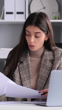 Modern ofiste çalışırken, belgeleri analiz eden ve mali strateji planlayan heyecanlı, genç, beyaz bir kadın. Dikey video.