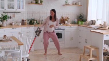 Heyecanlı orta yaşlı beyaz hamile kadın mutfağı süpürüyor ve müzik eşliğinde dans ediyor. Ev temizliği ve temizlik görevlerinin sürdürülmesi kavramı.