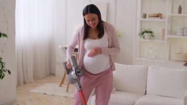 Hamile, gülümseyen, orta yaşlı, ev işleri yapan, yerleri süpüren, her gün temizlik yapan beyaz bir kadın..