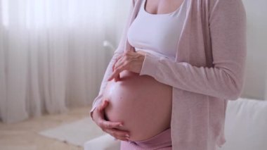 Orta yaşlı hamile bir beyaz kadının oturma odasında bebek çarpıntısı çekerken yakın plan fotoğrafı. Hamilelik kavramı, çocuk bekleyen ve sevecen..