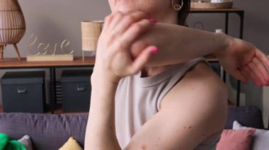 Kafkas kökenli orta yaşlı bir kadının oturma odasında omuz ve kollarını esnetme egzersizi yaparken yakın çekim. Isınma ve kas antrenmanı..