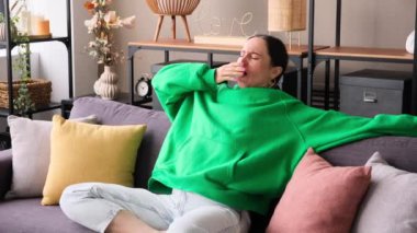 Yorgun ve uykulu orta yaşlı beyaz kadın esniyor ve esniyor, evdeki kanepede uzanıyor. Sıkıntı kavramı, yorgunluk, ilgisizlik..