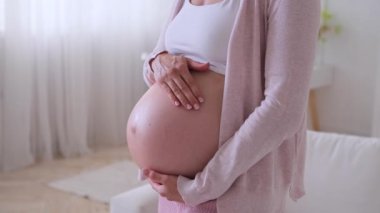 Hamile, orta yaşlı, beyaz bir kadının hamilelik sarsıntısını dindirdiği ve evde gelecekteki anneliğin tadını çıkardığı yakın çekim. Hamilelik ve beklenti kavramı.