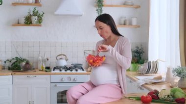 Neşeli orta yaşlı, beyaz hamile kadın evcil mutfakta lezzetli sebze salatası yiyor. Hamilelik ve taze yemek kavramı.