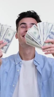 Neşeli, genç, beyaz bir adam para kazanıyor, para banyosu yapıyor, zenginliği beyaz arka planda kutluyor. Yatırım kavramı ve kazanç. Dikey video.