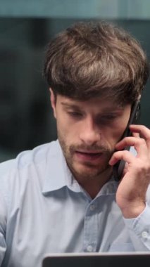 Ofiste çalışırken iş konuşmak için akıllı telefonu kullanan orta yaşlı, güler yüzlü bir adam. Müşteri ile uzaktan konsültasyon kavramı. Dikey video.