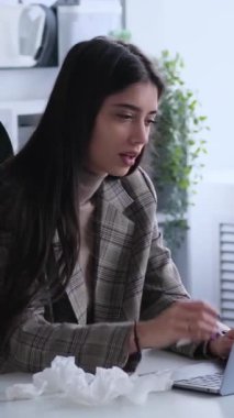Ofiste dizüstü bilgisayarla çalışırken solunum hastalığından muzdarip üzgün beyaz kadın ofis çalışanı. Dikey video.