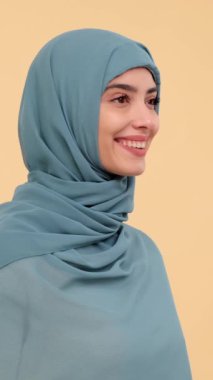 Bej arka planda tesettür takan gülümseyen ve heyecanlı bir Arap kadının profil portresi. Olumlu insanlar kavramı. Dikey video.