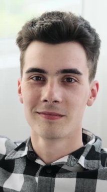 Öfkeli Kafkasyalı genç bir adam cep telefonunu internet üzerinden mesaj atmak için kullanıyor. Ev oturma odasında boş vakit geçiriyor. Dikey video.