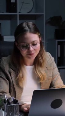 Dost canlısı, genç, yetişkin, Kafkas ofis çalışanı. Akşam ofisinde, bilgisayarla çalışıyor ve başarıyı kutluyor. Dikey video.