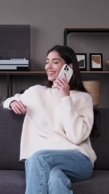 Güler yüzlü kadın evde cep telefonu kullanarak diyalog ya da iletişim kuruyor. Sohbet ya da telekomünikasyon kavramı. Dikey video.