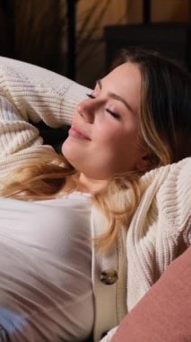 Tembel ve mutlu Kafkasyalı genç kadın akşam evde boş vakit geçirirken kanepede dinleniyor ve dinleniyor. Dikey video.