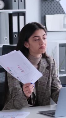 Ofiste belgelerle uğraşırken kollarını açıp omuz silken yardıma muhtaç beyaz kadın. Dikey video.
