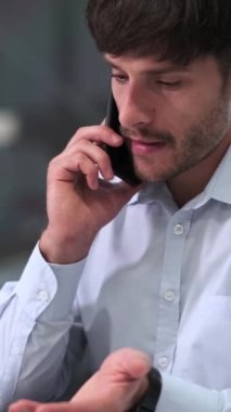 Konsantre olmuş, beyaz, orta yaşlı, serbest çalışan bir erkek, ofiste çalışırken müşterisiyle iş görüşmesi ya da iş görüşmesi yapar. Dikey video.