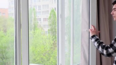 Ciddi bir beyaz adam ev oturma odasındaki havalandırmadan sonra plastik pencereyi açtı. Soğuk hava, temiz hava konsepti.