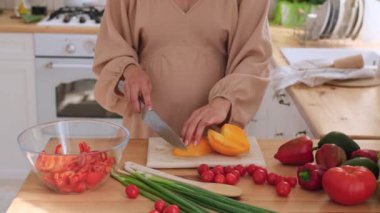 Hamile, orta yaşlı, yemek pişirme rutini yapan ve mutfakta sebze salatası hazırlayan beyaz bir kadın. Sağlıklı ve taze yiyecek kavramı.