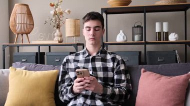 Neşeli beyaz adam cep telefonu kullanıyor ve evdeki oturma odasında sosyal medyada mesajlaşıyor. Boş vakitlerde internet taraması ve dinlenme.