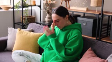 Bunalımlı orta yaşlı beyaz kadın baş ağrısı çekiyor. Oturma odasındaki kanepede tek başına oturuyor. Gerilim, hastalık, hastalık. Duygusal stres kavramı.