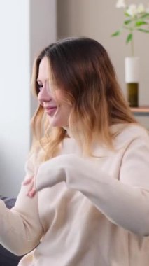 Kafkasyalı genç bir kadın müzik eşliğinde dans ediyor ve eğleniyor. Boş zamanlarını evde, kanepede geçiriyor. Zevk ve eğlence kavramı. Dikey video.