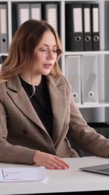 Ofiste çalışırken çevrimiçi sohbete katılan kızgın Kafkasyalı genç kadın. Uzaktan video çağrısı konsepti. Dikey video.