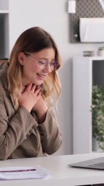 Neşeli Kafkasyalı genç iş kadını iyi haberler alıyor ve ofiste dizüstü bilgisayarla çalışıyor. Başarı ve memnuniyet kavramı. Dikey video.