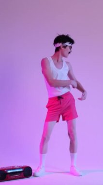 Heyecanlı beyaz bir genç adam müzik eşliğinde dans ediyor, boş zamanlarını geçiriyor ve mor arka planda eğleniyor. Parti ve eğlence anlayışı. Dikey video.