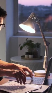 Uzaktan kumandalı, bilgisayarla çalışan, gazete okuyan, akşam evde iş planlayan odaklanmış beyaz bir adam. Dikey video.