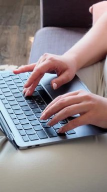 Dizüstü bilgisayarda daktilo kullanan, evdeki kanepede oturan bir kadının yakın çekim görüntüsü. İnternet veya internet aktiviteleri kavramı. Dikey video.