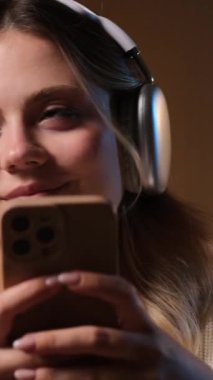 Neşeli, genç, beyaz bir kadının gece yarısı evinde cep telefonuyla boş vakitlerini internette geçirdiği portreyi yakından çek. Dikey video.