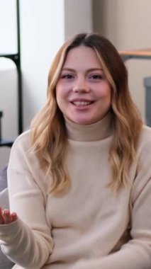 Dost canlısı genç beyaz kadın blogcu sosyal medya için internetten yayın yapıyor ya da evdeki oturma odasında video kaydediyor. Dikey video.