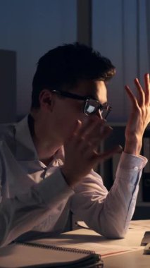 Gece geç saatlerde ofiste çalışırken dizüstü bilgisayar kullanarak internete liderlik eden Kafkasyalı genç bir ofis çalışanı. Dikey video.