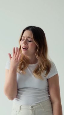 Sıkılmış beyaz kadın esniyor ve esniyor, beyaz arka planda duruyor. Can sıkıntısı, yorgunluk ya da aşırı çalışma kavramı. Dikey video.