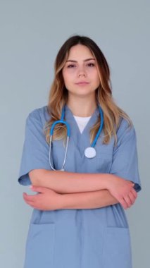 Mavi arka planda çapraz kollarla duran ciddi bir doktor ya da hemşirenin portresi. Konsantre tıp uzmanı. Dikey video.