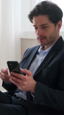 Mola sırasında akıllı telefon harcayan ve ofiste kahve içen mutlu, genç, beyaz bir adam. Çevrimiçi eğlence kavramı. Dikey video.