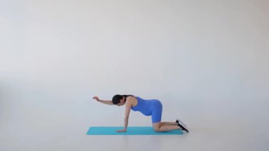 Mutlu ve sağlıklı, orta yaşlı, beyaz arka planda yoga seansı sırasında omuzlarını dört ayak üstüne uzatan orta yaşlı, hamile bir kadın. Annelik süresince egzersiz..