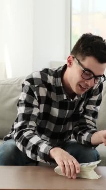 Sosyal medyada akıllı telefon kullanarak mesajlaşırken, evde boş zaman geçirirken, düşünceli beyaz bir genç adamın fikri. Dikey video.