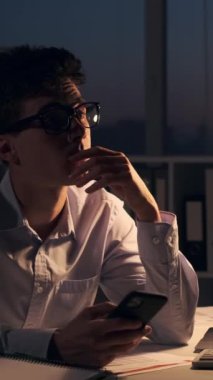 Çok çalışan Kafkasyalı genç iş adamı, ara verildiğinde cep telefonu ve internet kullanarak dinleniyor. Dikey video.