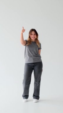 Beyaz arka planda duran, onaylama ya da onaylama jesti gibi, tatmin olmuş, genç, beyaz bir kadın. Dikey video.