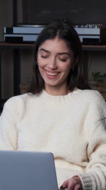 Neşeli, genç, beyaz bir kadın evde dizüstü bilgisayarla vakit geçiriyor. İnternette eğlence ve boş zaman. Dikey video.