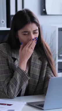 Yorgun beyaz kadın ofis çalışanı ofiste çalışırken esniyor ve esniyor. Sıkıntı ya da yorgunluk kavramı. Dikey video.