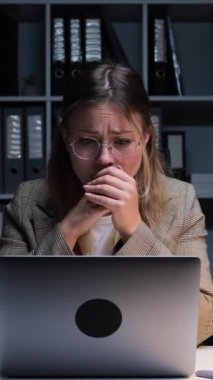 Gergin, genç, beyaz bir kadın gece yarısı ofisinde dizüstü bilgisayarla çalışırken hata ya da kayıptan bunalmış. Dikey video.