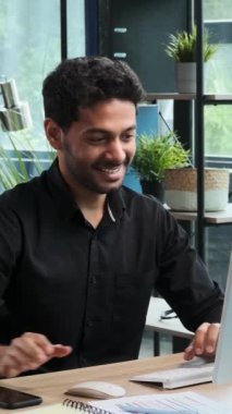 Ofiste çalışırken cep telefonu kullanan heyecanlı bir Orta Doğulu genç iş adamı. İletişim ve mesajlaşma kavramı. Dikey video.