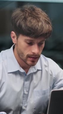 Yoğunlaşmış Kafkasyalı orta yaşlı erkek çalışan dizüstü bilgisayarla çalışıyor, iş yönetiyor ve ofiste kahve içiyor. Dikey video.