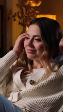 Akşam evde boş vakit geçirirken, gülümseyen genç, beyaz bir kadın televizyon seyrediyor. Ev içi boş zaman kavramı. Dikey video.