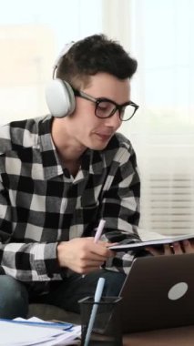 Kızgın, genç, beyaz bir adam, oturma odasından ders çalışırken belgeleri yırtıyor. Stres ve sorun kavramı. Dikey video.