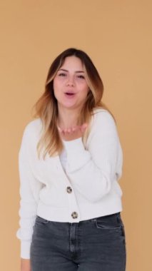 Arkadaş canlısı, genç, beyaz bir kadın bej arka planda hava öpücüğü veriyor ve dans ediyor. Eğlence ve romantizm kavramı. Dikey video.