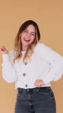 Müzik eşliğinde dans eden, eğlenen, bej arka planda duran beyaz bir kadın. Parti ya da disko konsepti. Dikey video.