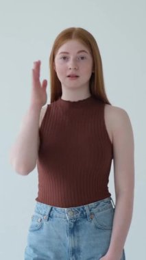 Hoşnut olmayan kızıl saçlı beyaz kız beyaz arka planda el hareketi yapıyor. Hayal kırıklığı, sıkıntı, utanç kavramı. Dikey video.